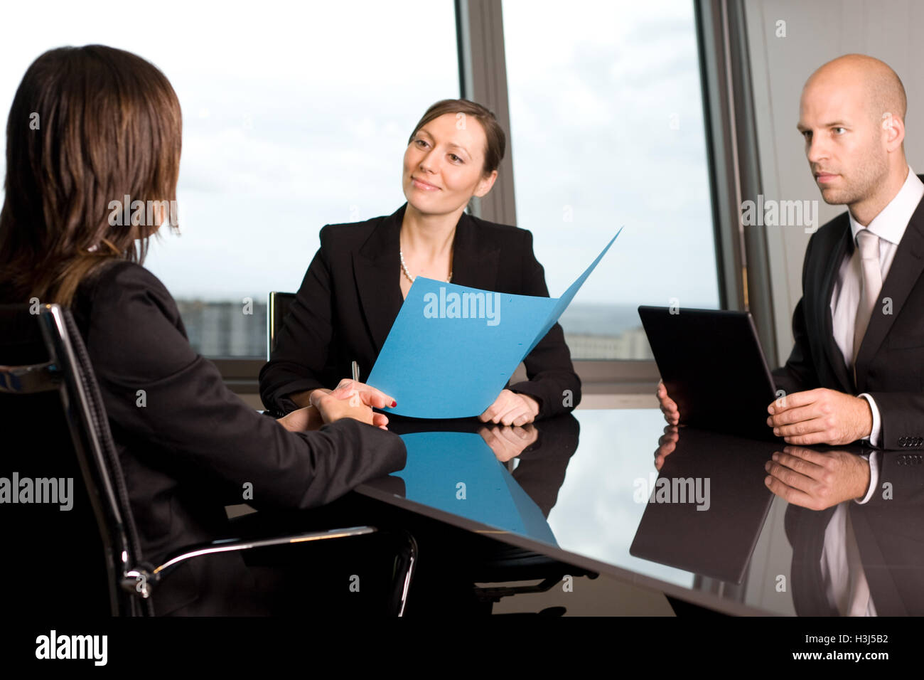 Job interview with three persons in dark business clothes in a panoramic office Stock Photo