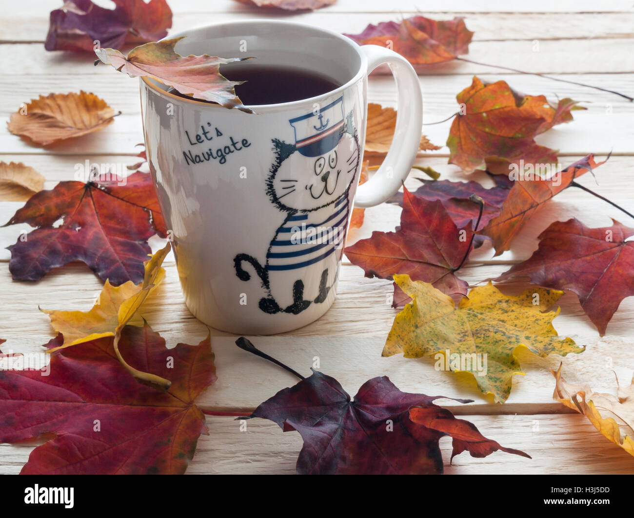 Beautiful and colorful autumn leaves and white cup of tea standing on a table made of wooden plank Stock Photo