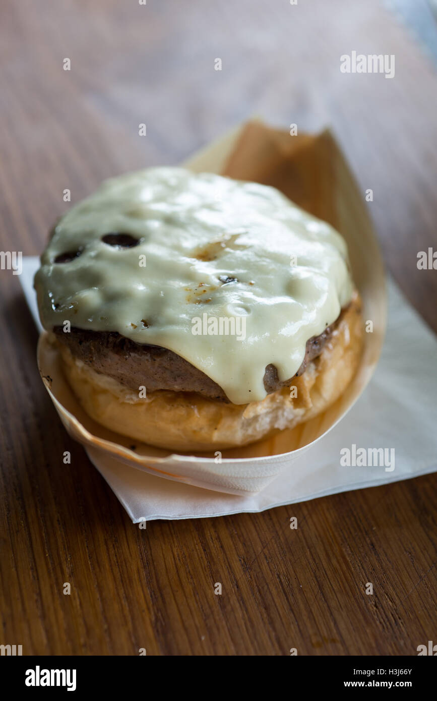 cheeseburger on half a bread bun in a metallic food tray ontop of a white napkin on a wooden surface Stock Photo