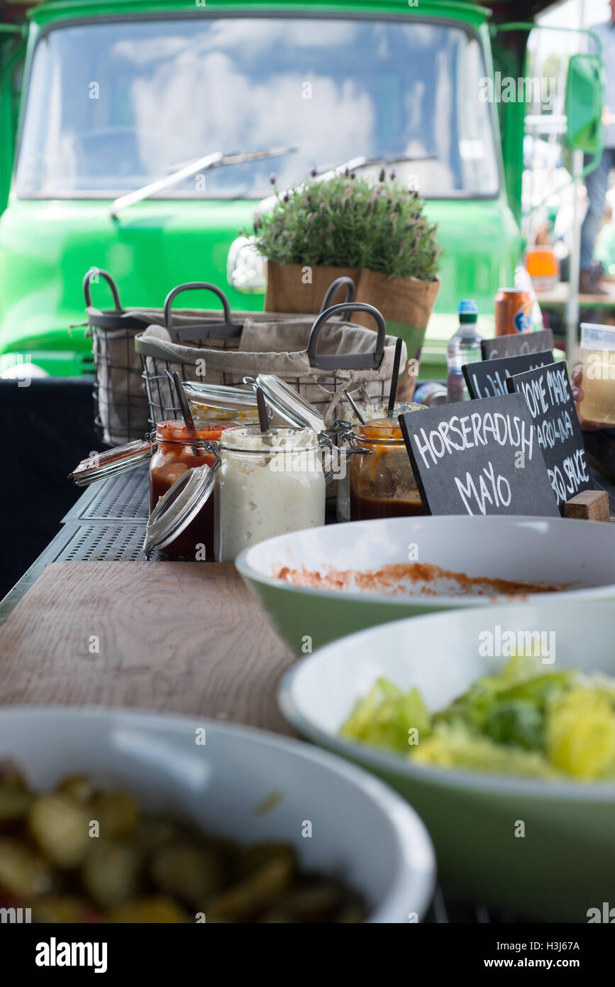 green plastic bowls with lettuce and other burger toppings, jars of sauce and pots of herbs on a wooden table with a bright gree Stock Photo