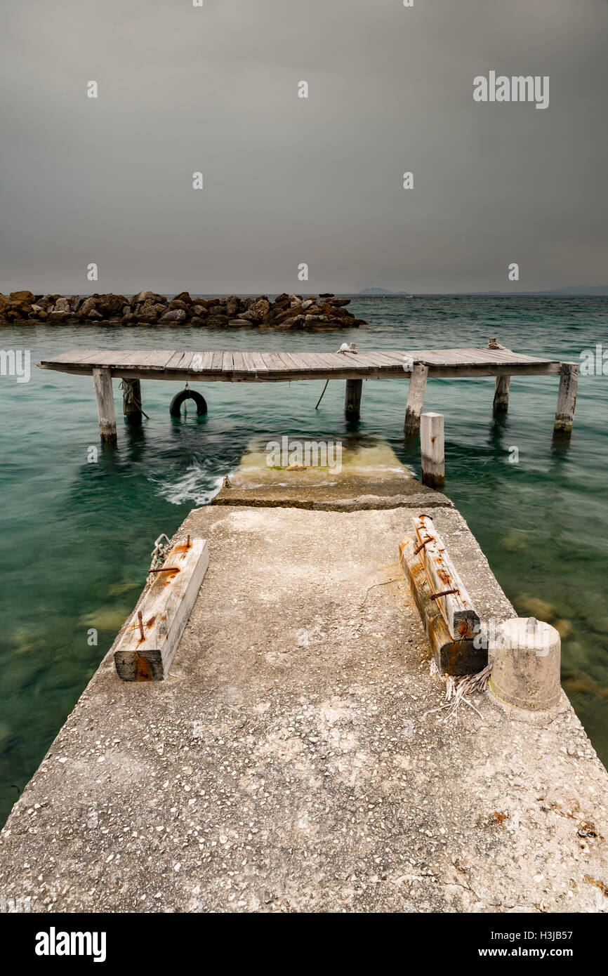 A damaged and dangerous jetty collapses into the sea in Greece as a storm cloud blows in. Stock Photo
