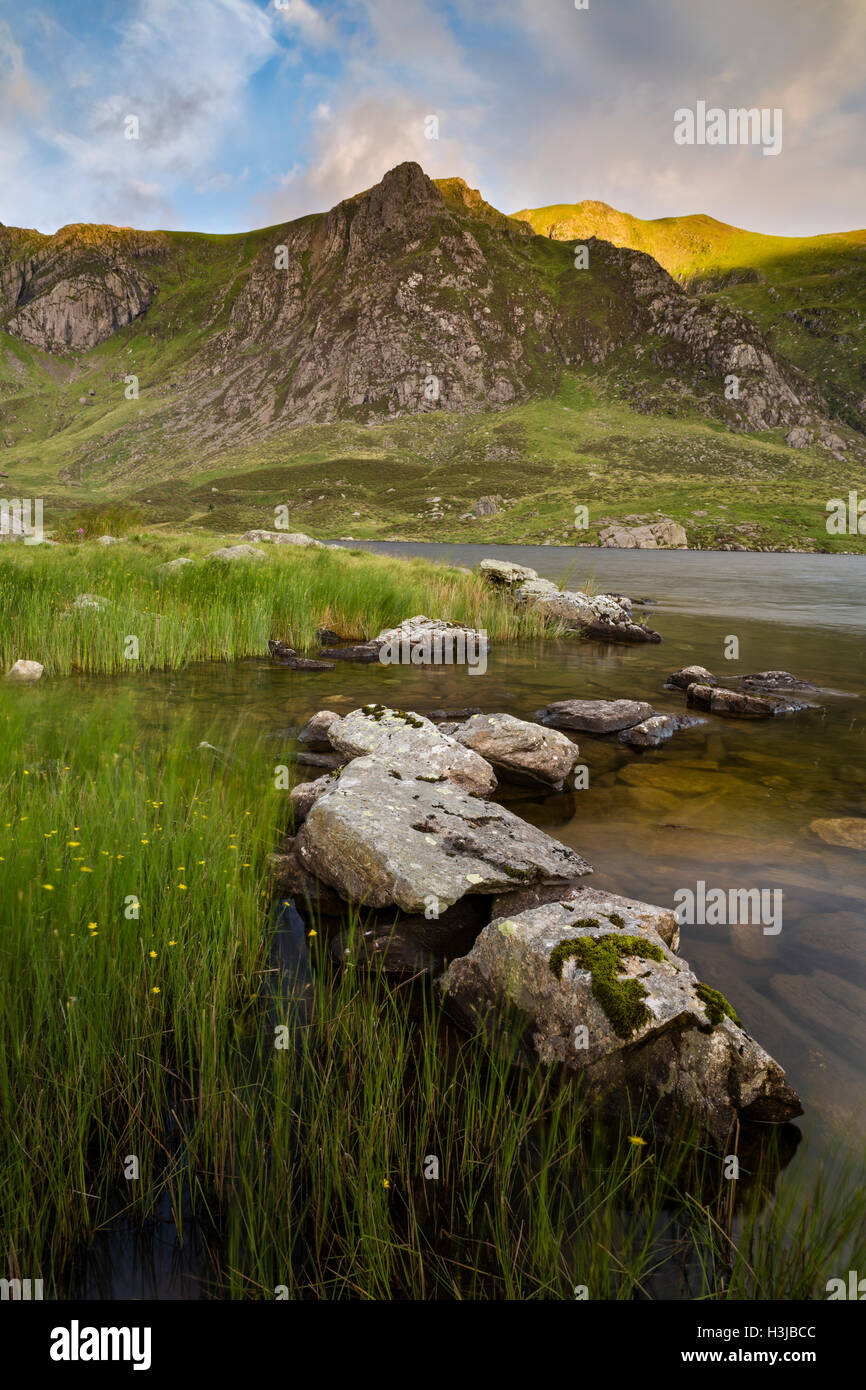 Llyn Idwal, Snowdonia, stands beneath Castell y Geifr and Y Garn, which is bathed in the golden light of sunrise. Stock Photo