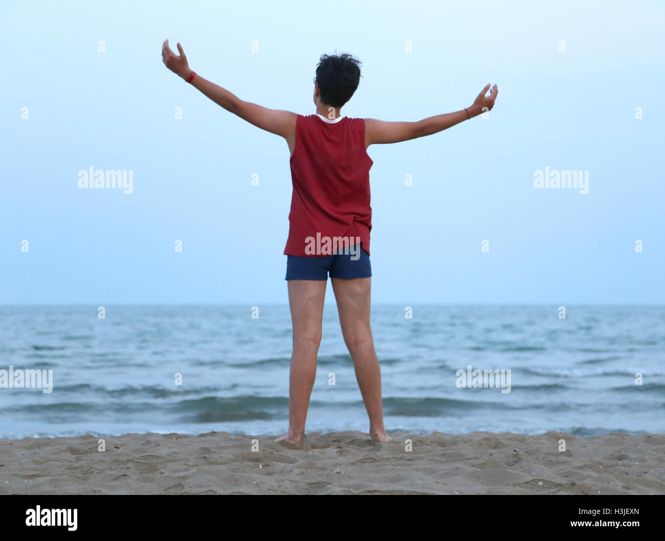 young guy with raised arms on the seashore at dusk Stock Photo
