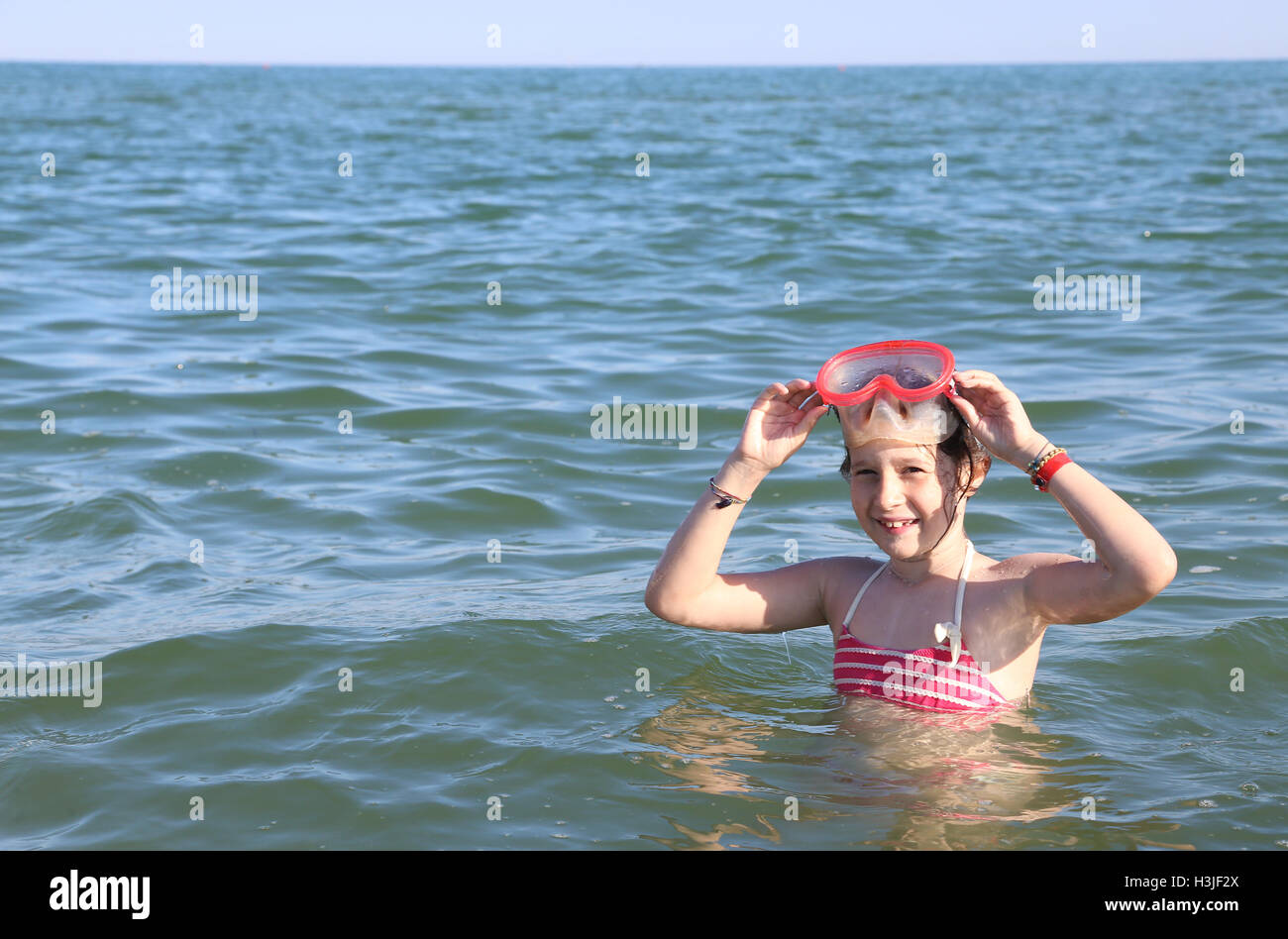 beautiful little child smiling while playing with the diving mask in the sea Stock Photo