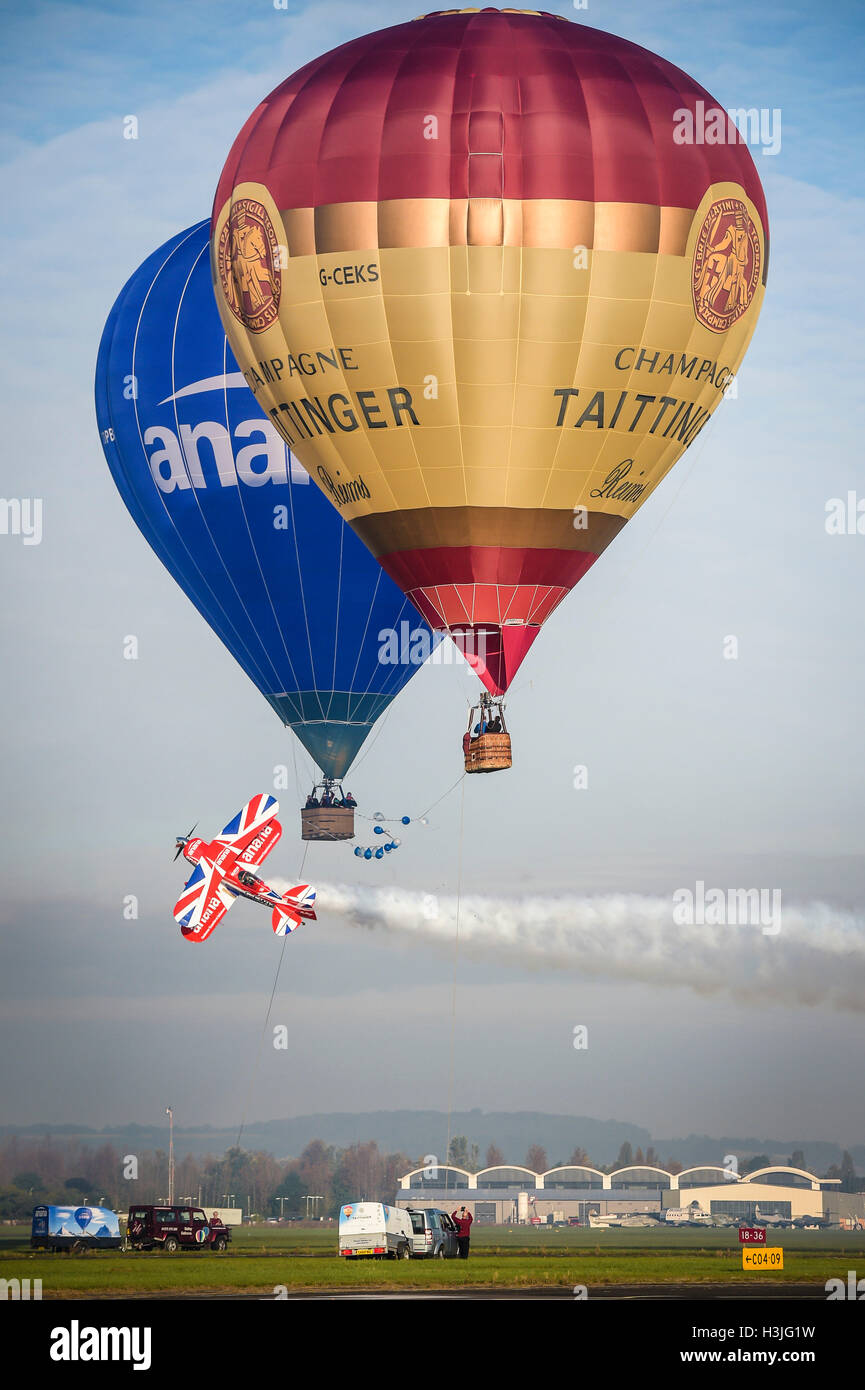 A Pitts Special S2S stunt plane performs the worlds first ever 'knife edge' between two hot air balloons, cutting a ribbon as it passes between them just above the ground at Gloucester airport. Stock Photo