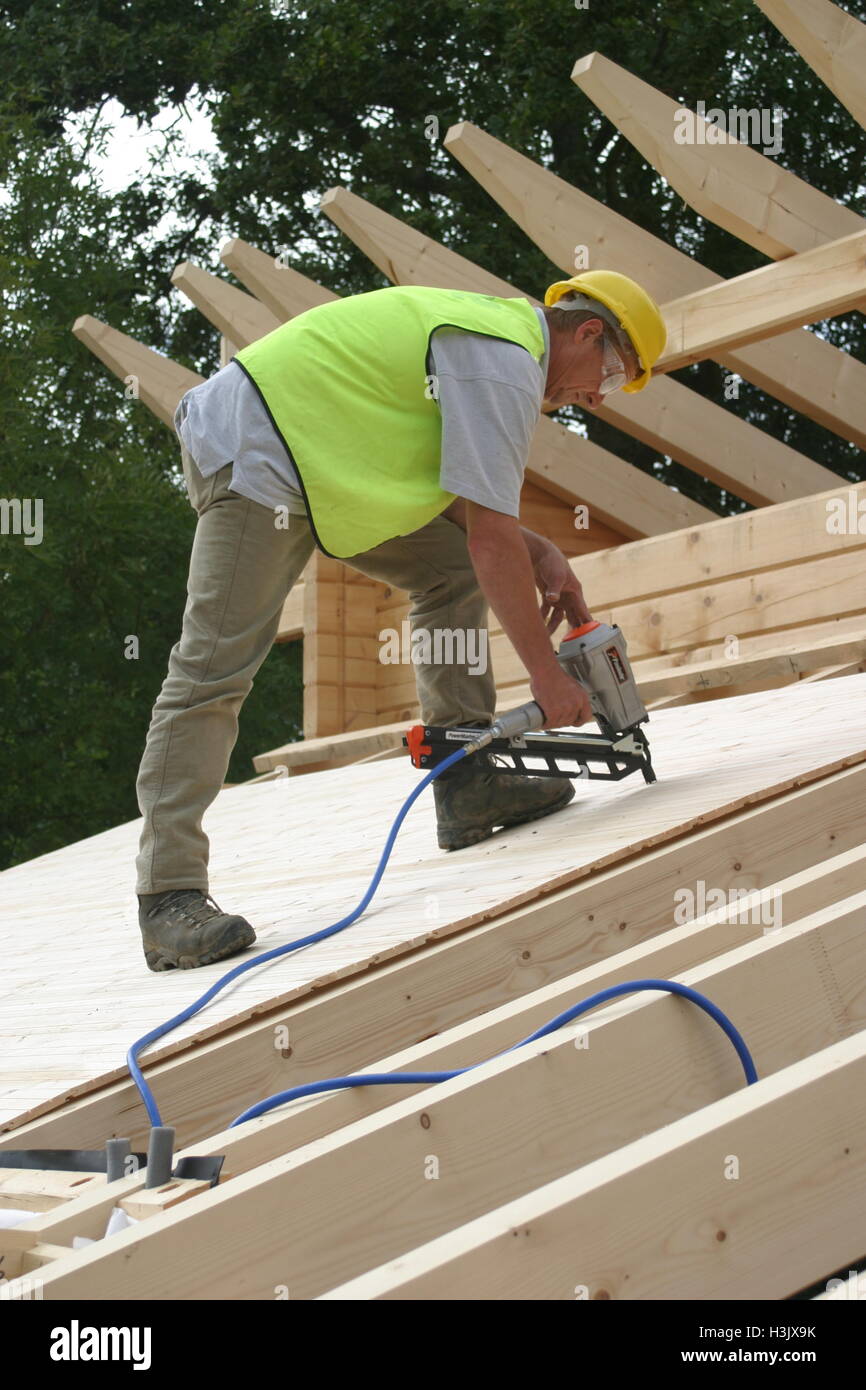 A worker uses an airpowered nail gun to fasten roofing boards on a