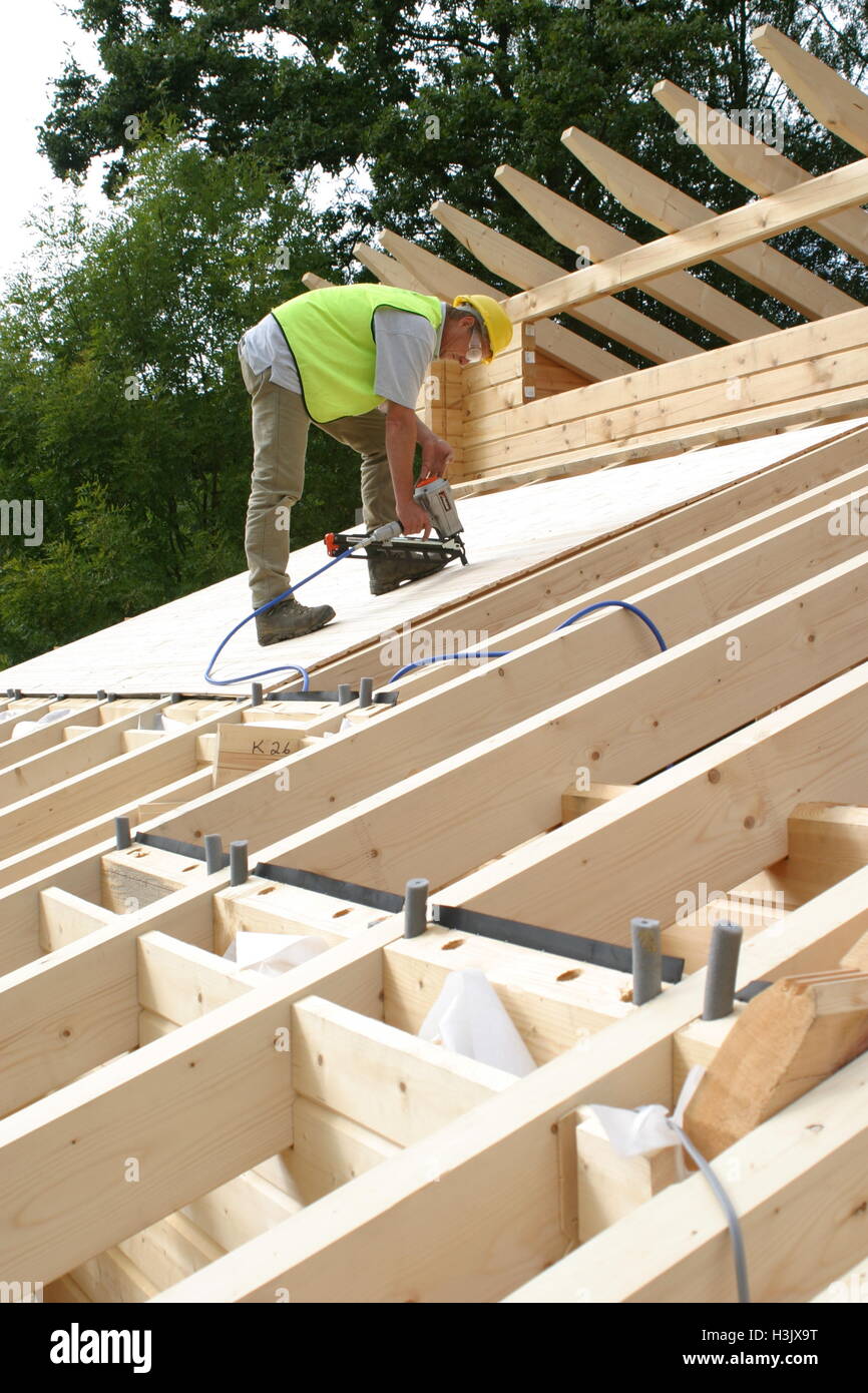 A worker uses an airpowered nail gun to fasten roofing boards on a timber selfbuild house in