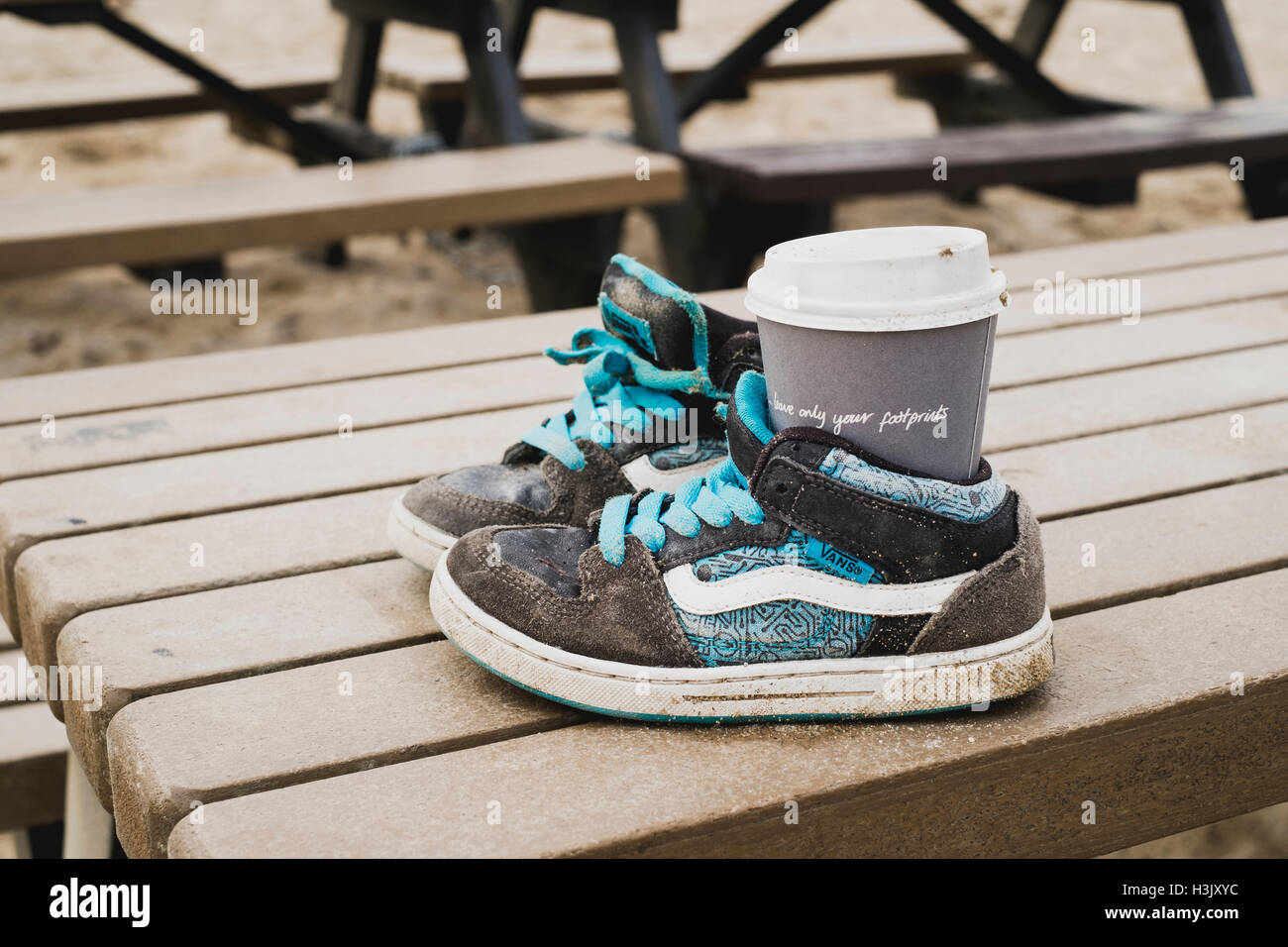 Ironic that a cup with 'leave only footprints' - an anti-litter message, is left discareded in a pair of childrens shoes. Stock Photo