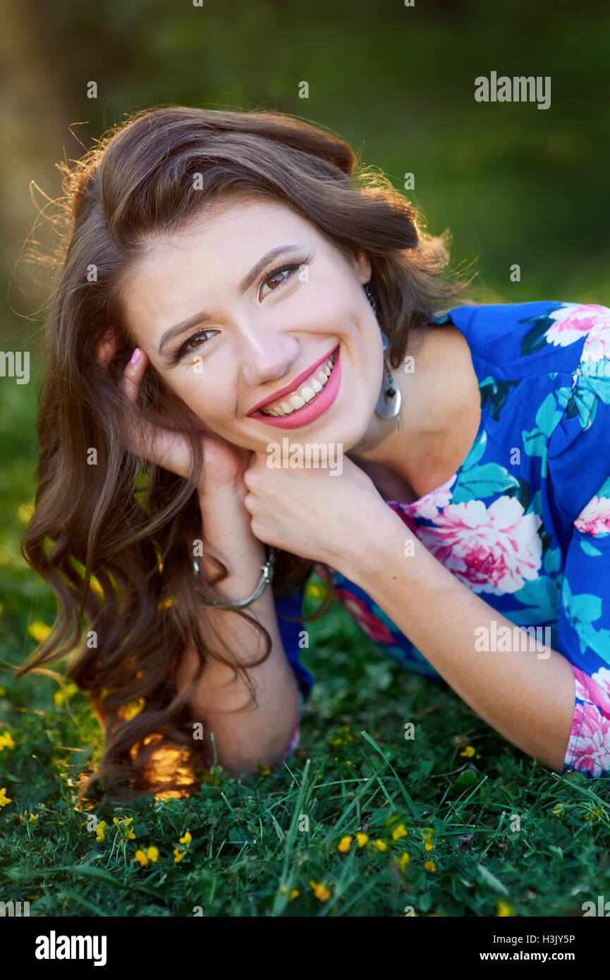 relaxed beautiful young woman in blue dress lying on grass Stock Photo
