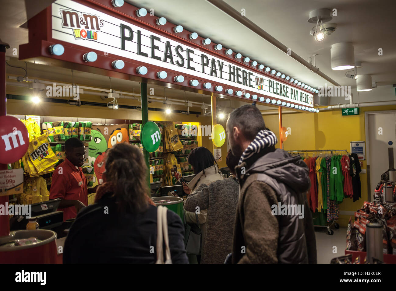 M&M store people waiting to pay for goods in front of the cash register under the sign 'please pay here' in London, UK Stock Photo