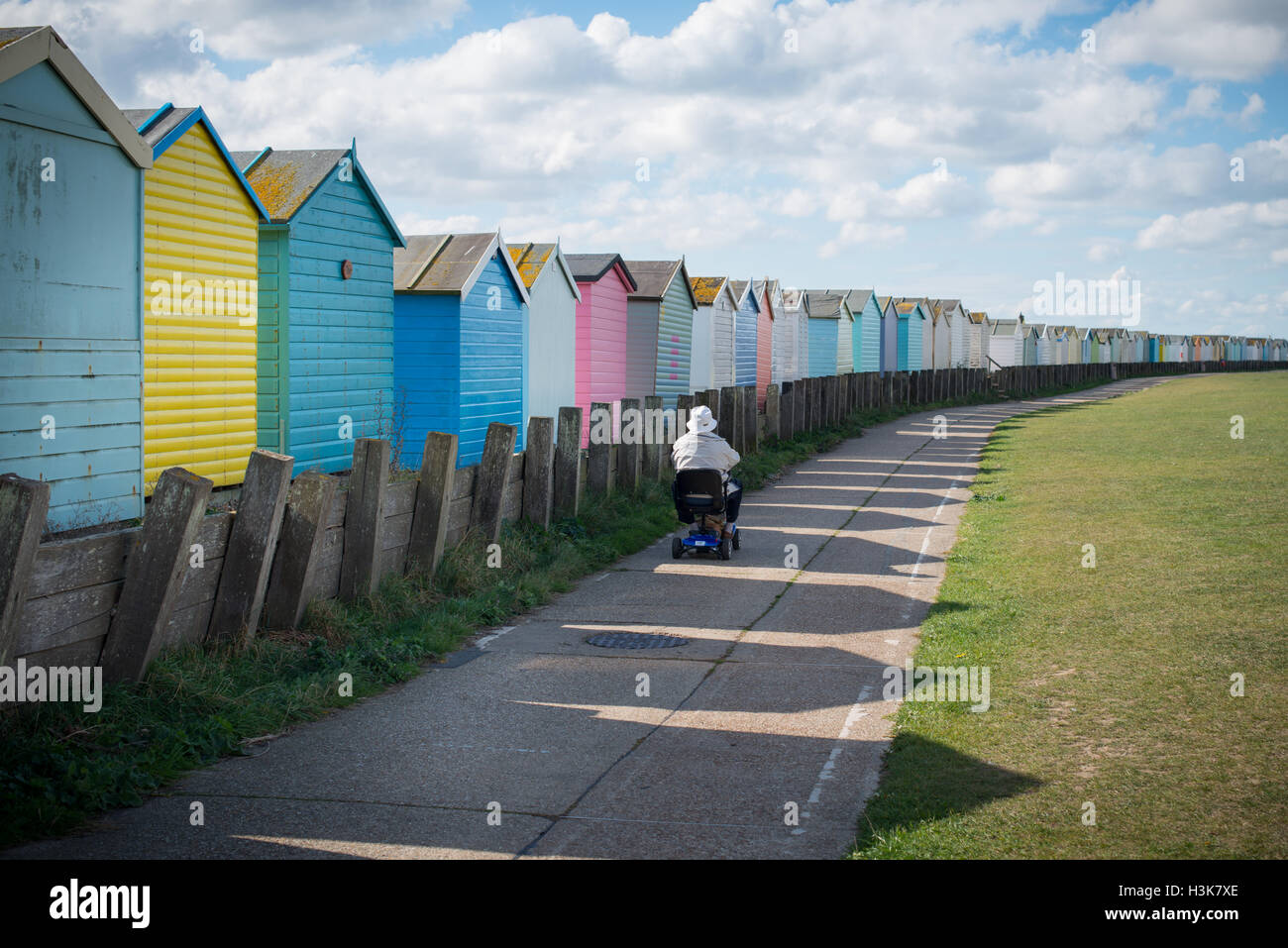 A man on a mobility scooter passes by colourful beach huts at Lancing