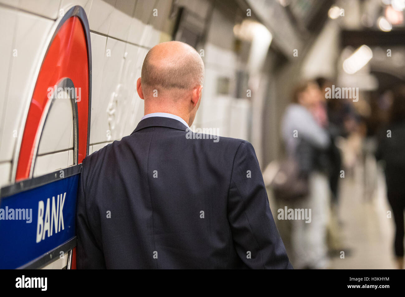 A man waiting for a train at Bank station on the London underground rear view with blurry background including logo roundel for transport for london Stock Photo