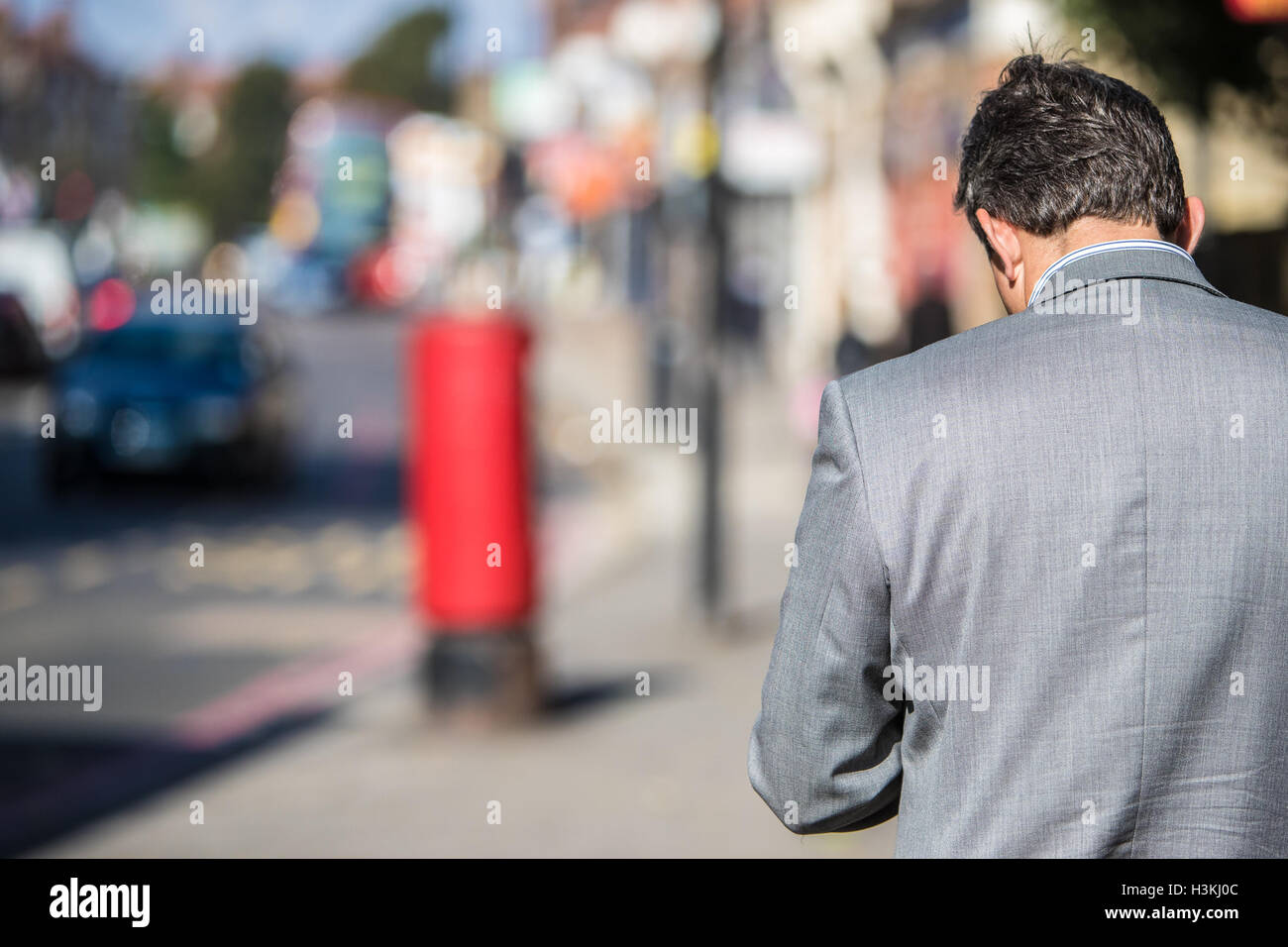 Suited man on British high street rear view red post box in background sunny day Stock Photo