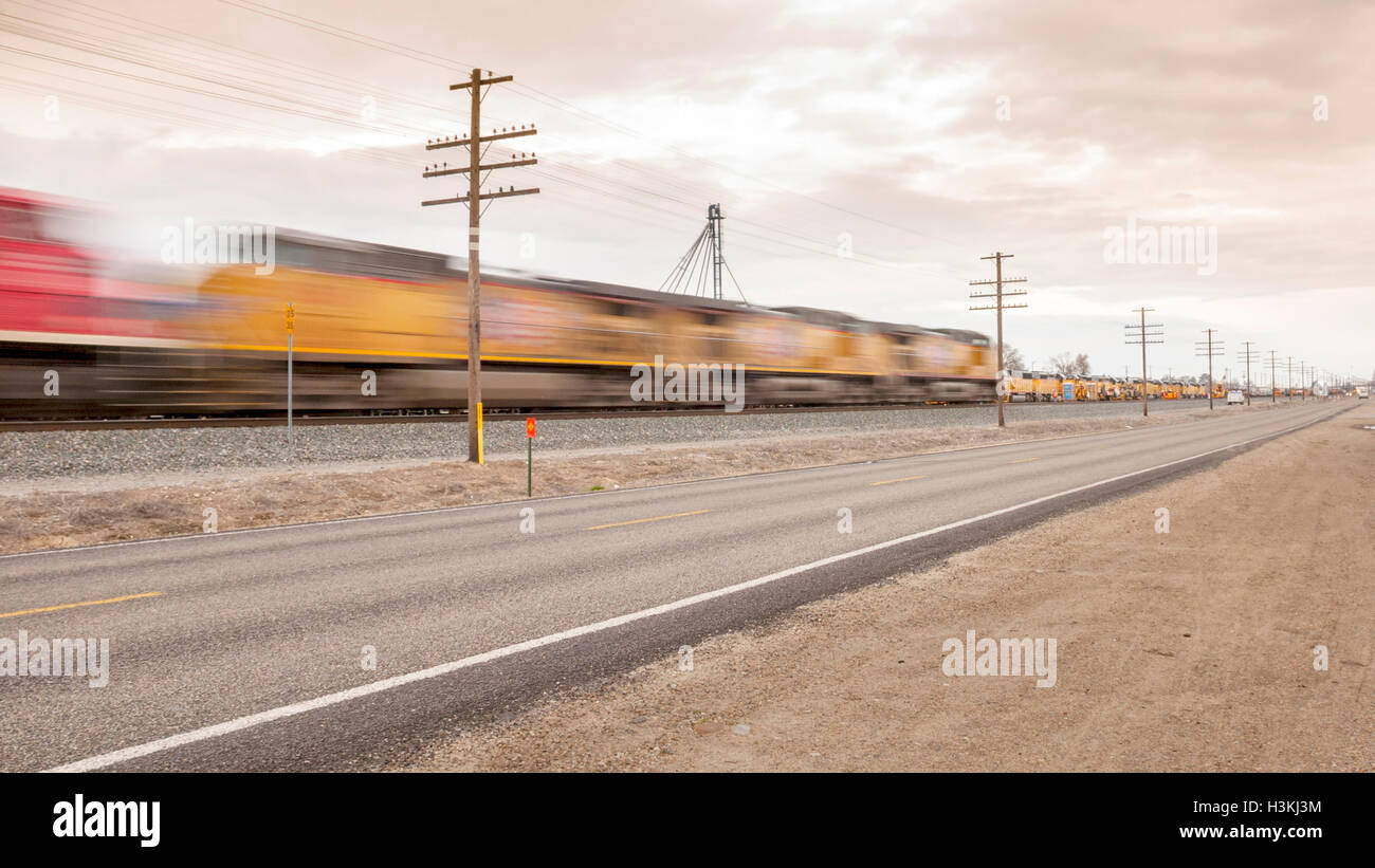 Speeding train blurs past a rural road Stock Photo