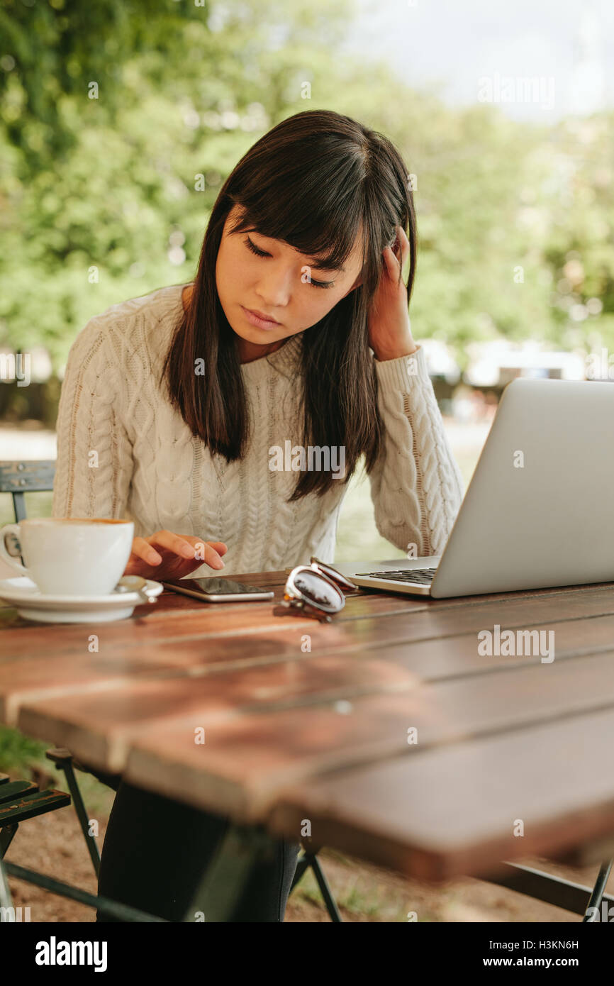 Beautiful young woman using mobile phone at cafe. Asian woman sitting at table outdoors using smartphone. Stock Photo