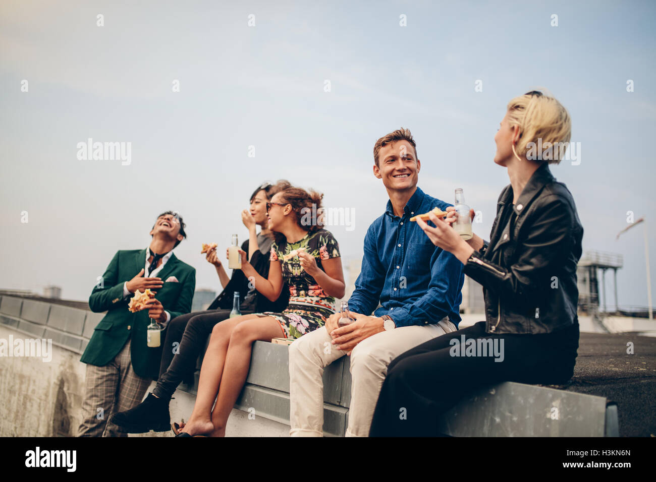 Group of friends partying on terrace, drinking and eating. Young men and women enjoying drinks on rooftop. Stock Photo