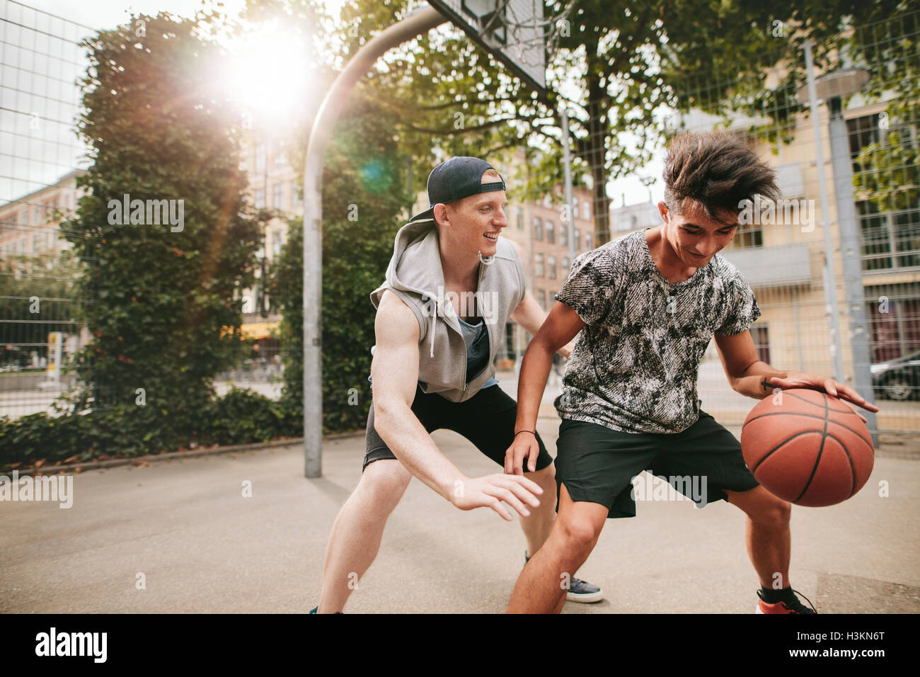Two young friends playing basketball on court outdoors and having fun. Streetball players having a basketball game. Stock Photo