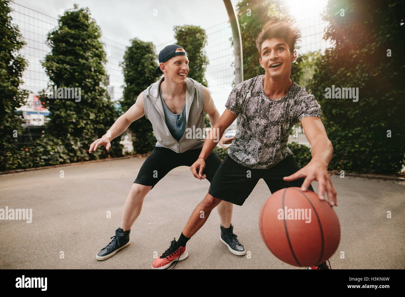 Two young friends playing basketball and having fun. Streetball players having a game of basketball on court outdoors. Stock Photo