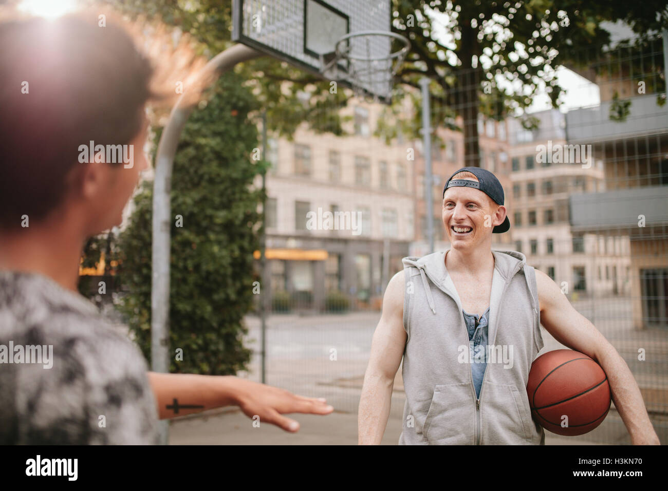 Young man with basketball on court talking with friend. Streetball players on court. Stock Photo
