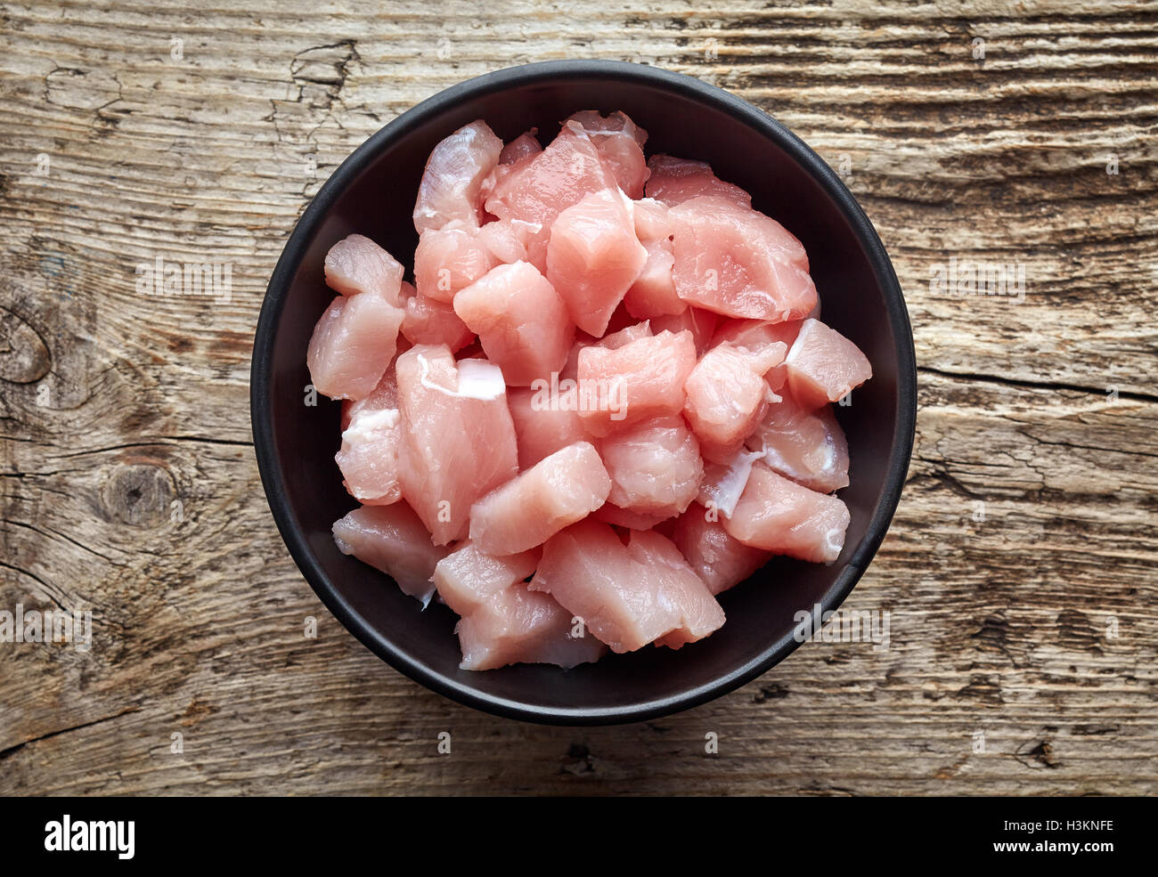 Raw cut meat chunks in black bowl on wooden table, top view Stock Photo