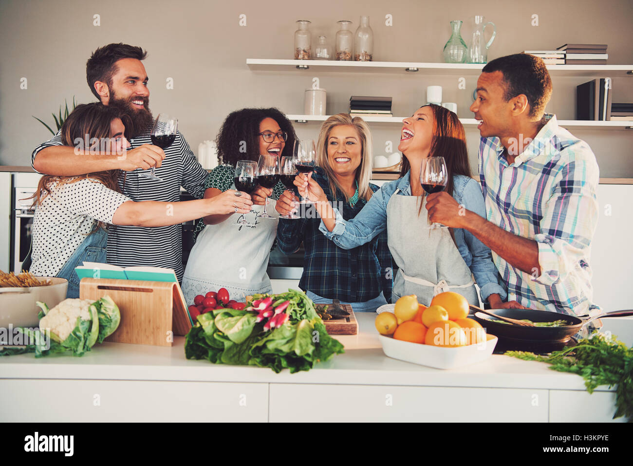 Fun group toasting wine glasses while cooking something to eat at large kitchen counter indoors Stock Photo