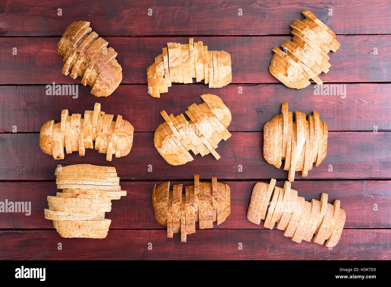 Top down view on nine sliced loaves of speciality wheat and white flour breads in staggered formation on dark stained wooden bac Stock Photo