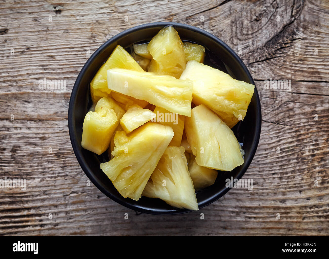 Bowl of canned pineapple chunks on wooden table, top view Stock Photo