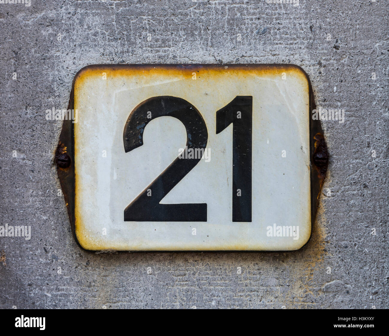 White rusty house number 21 on a grey wall. Stock Photo