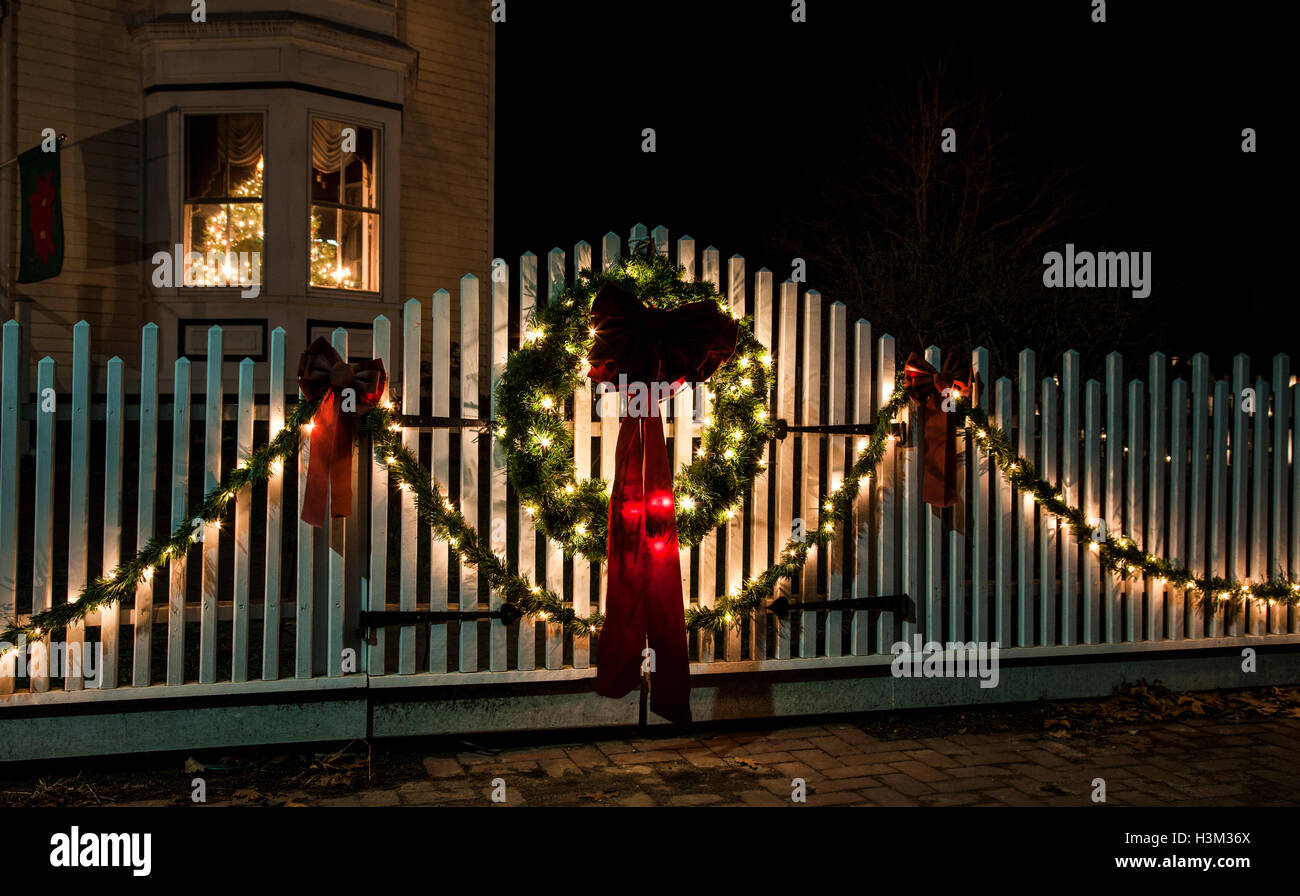 Night scene of a Christmas wreath and lights on a white picket fence
