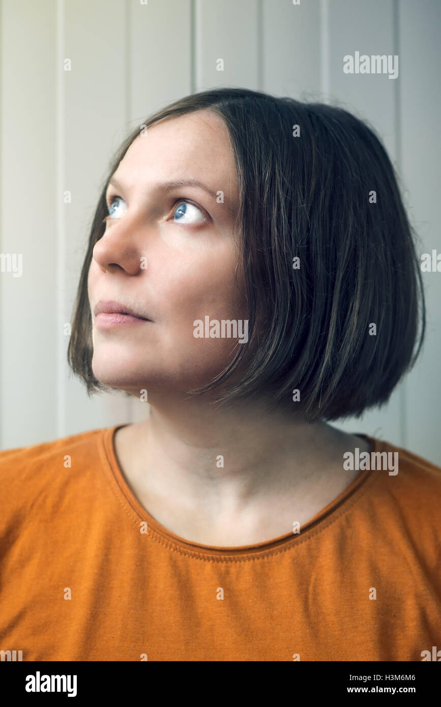 Hopeful beautiful young adult woman looking up to sunlight from window Stock Photo