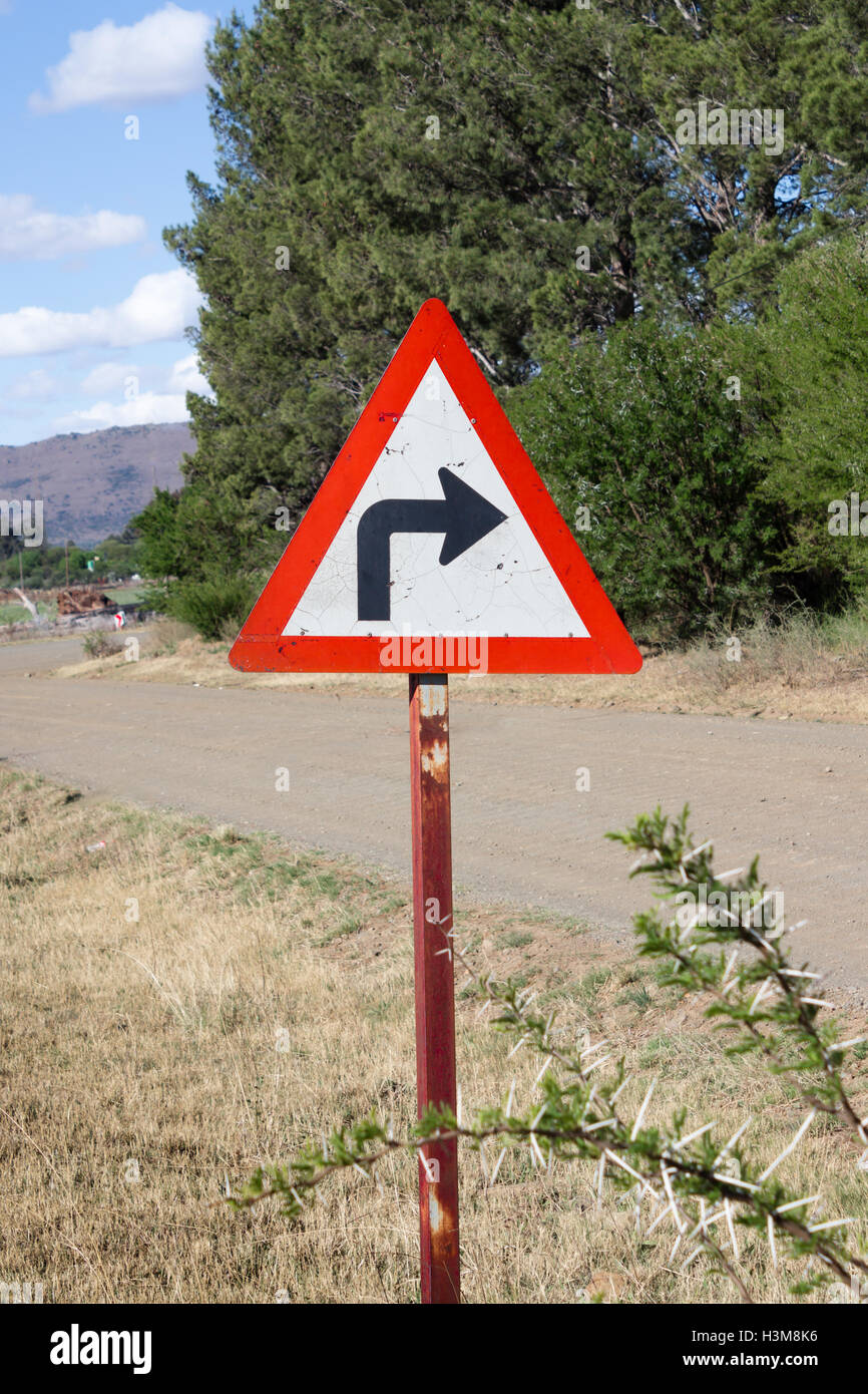 Weathered Sharp right hand turn sign next to rural road Stock Photo