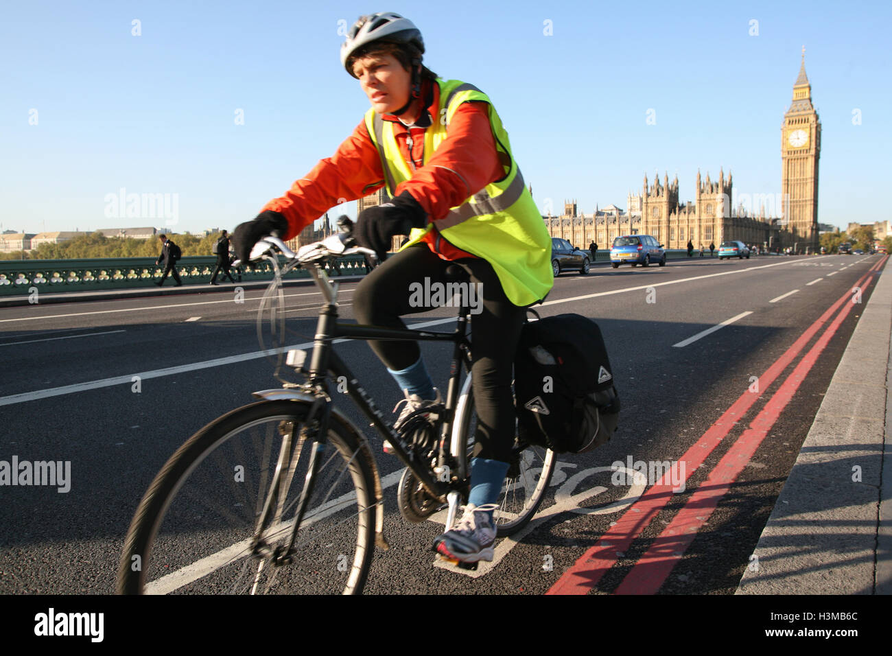 Cyclist rides along bicycle path on Westminster Bridge, with Houses of Parliament/Big Ben in the background. Sunny morning in Oc Stock Photo