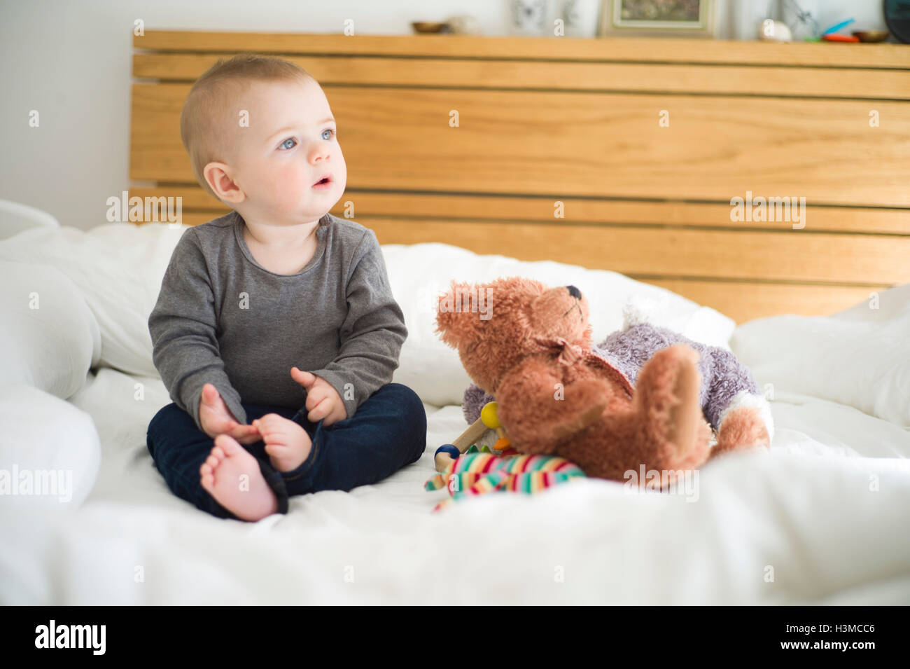 Baby girl sitting on bed with teddy bear looking away Stock Photo - Alamy