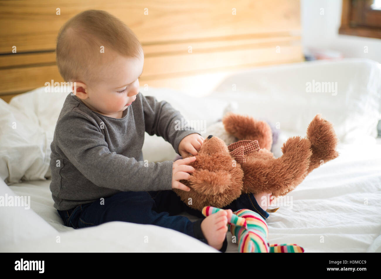 Baby girl sitting on bed playing with teddy bear Stock Photo - Alamy