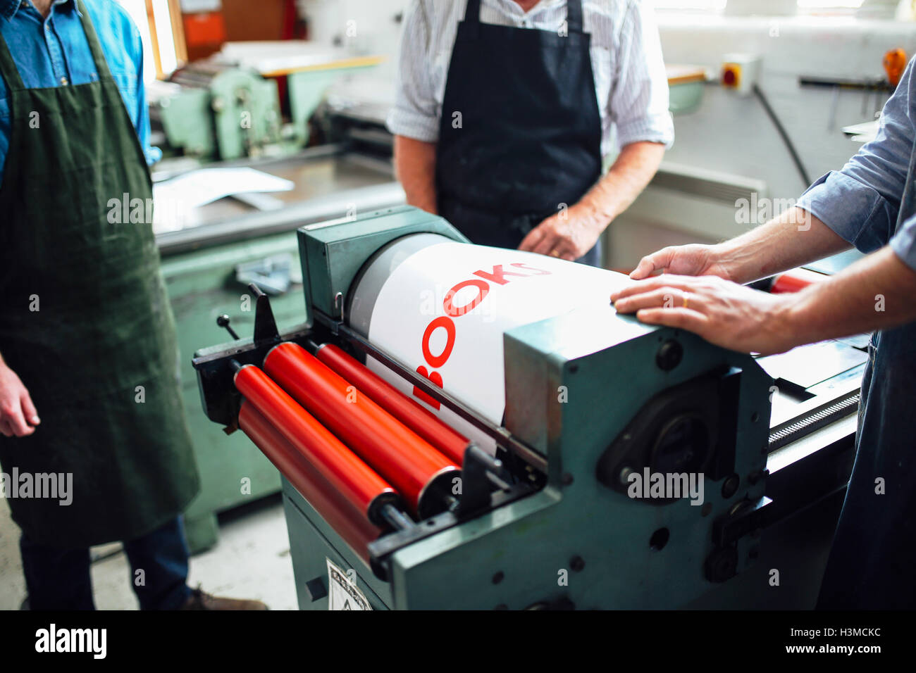Craftspeople being shown how to use letterpress machine in book arts workshop, mid section Stock Photo