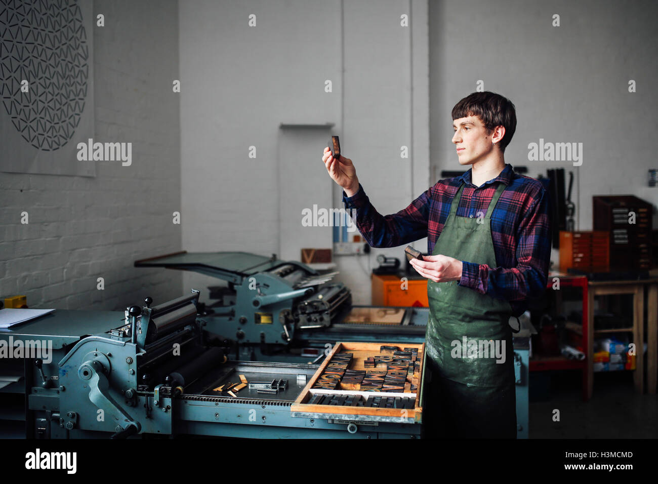 Young craftsman next to letterpress machine, holding up letter in print workshop Stock Photo