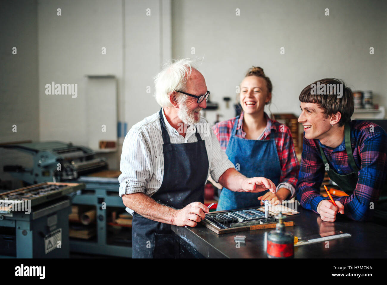 Senior craftsman laughing with young craftsman and craftswoman in letterpress workshop Stock Photo