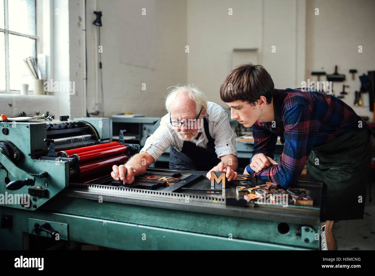 Senior craftsman teaching young craftsman to use letterpress machine in book arts workshop Stock Photo