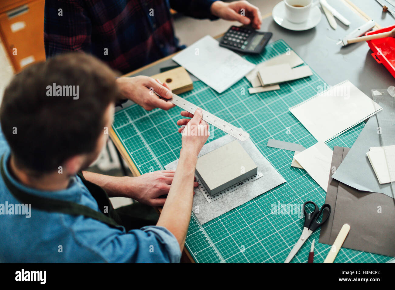 Young craftsman passing metal ruler to friend in print studio, elevated view Stock Photo