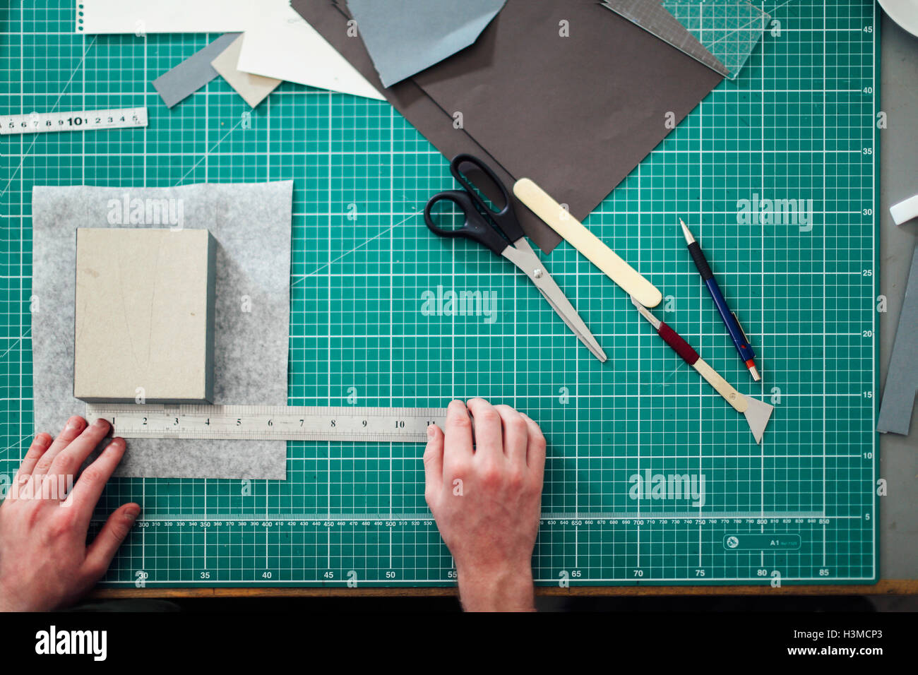 Overhead detail of hands, paper, cutting mat, ruler, scalpel and