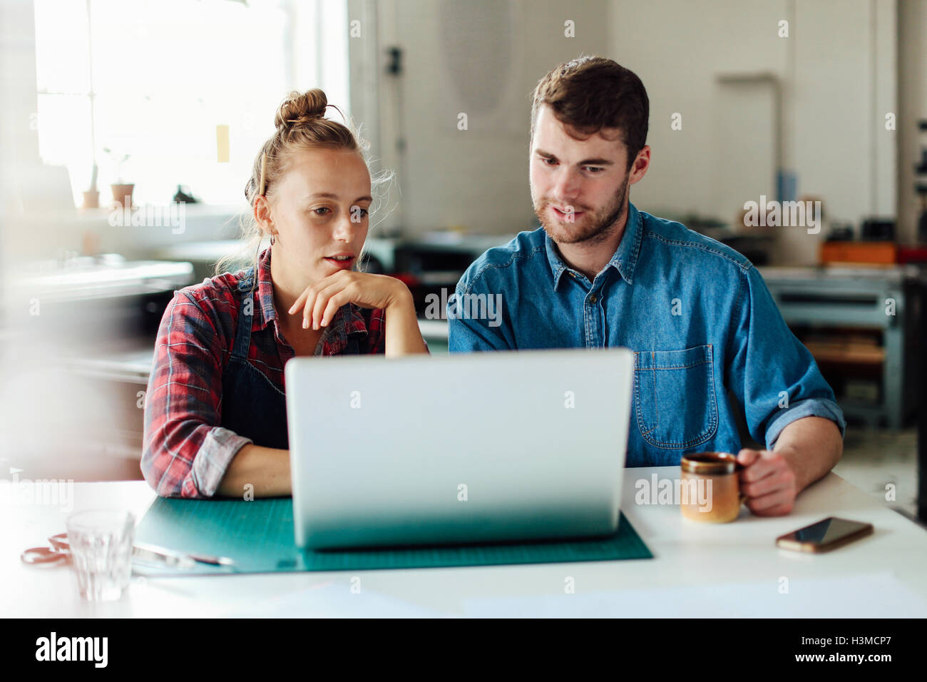 Young craftsman and craftswoman looking at laptop in print studio workshop Stock Photo