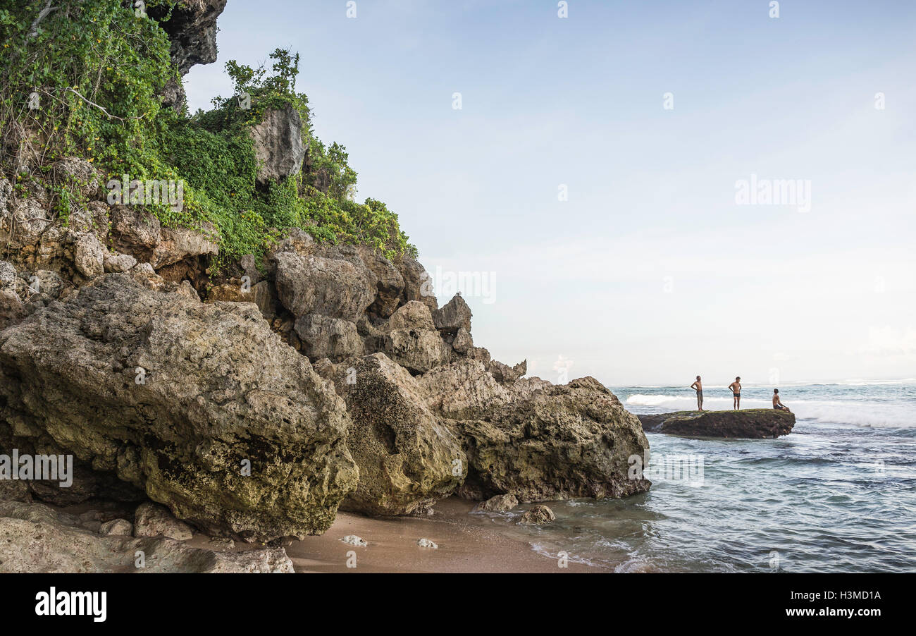 Three men on coastal rock at Panawa Beach, Bali, Indonesia Stock Photo