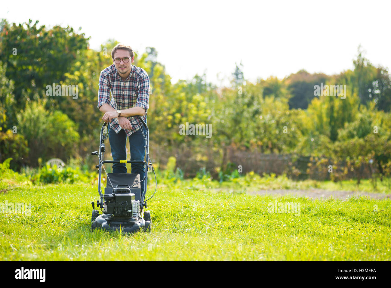 Young man is mowing the lawn on a nice sunny day. Stock Photo