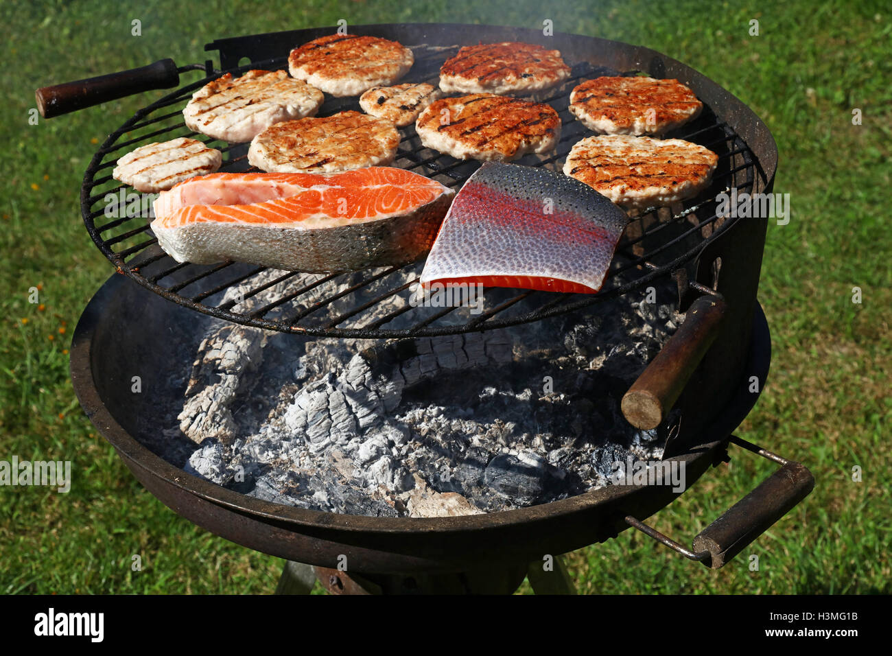 Chicken or turkey poultry meat barbecue grilled burgers for hamburger and salmon fish fillet steak prepared on bbq smoke grill o Stock Photo