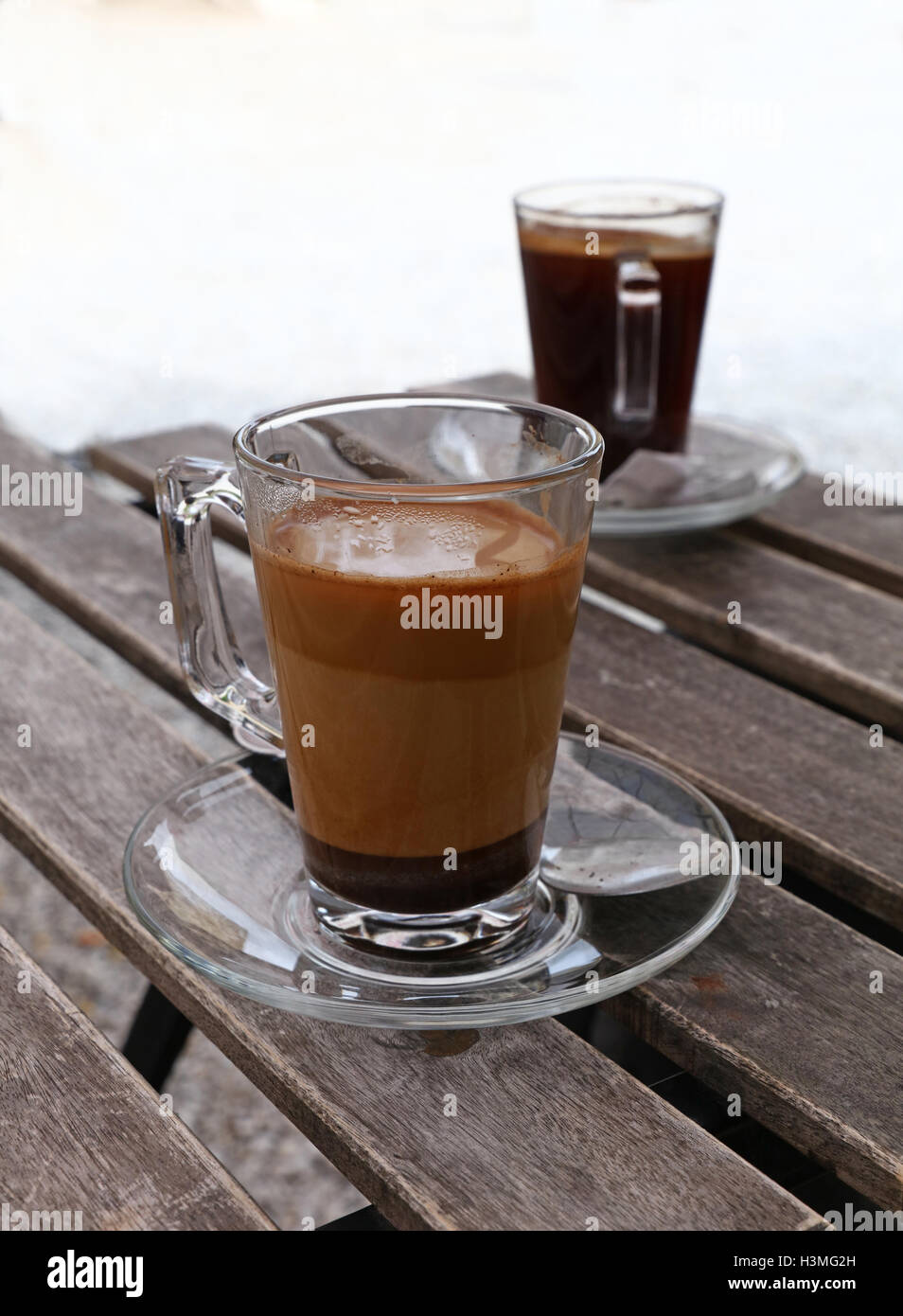 Two full Turkish freshly brewed natural ground coffee, black and with milk, in transparent full glass cups with saucer and metal Stock Photo