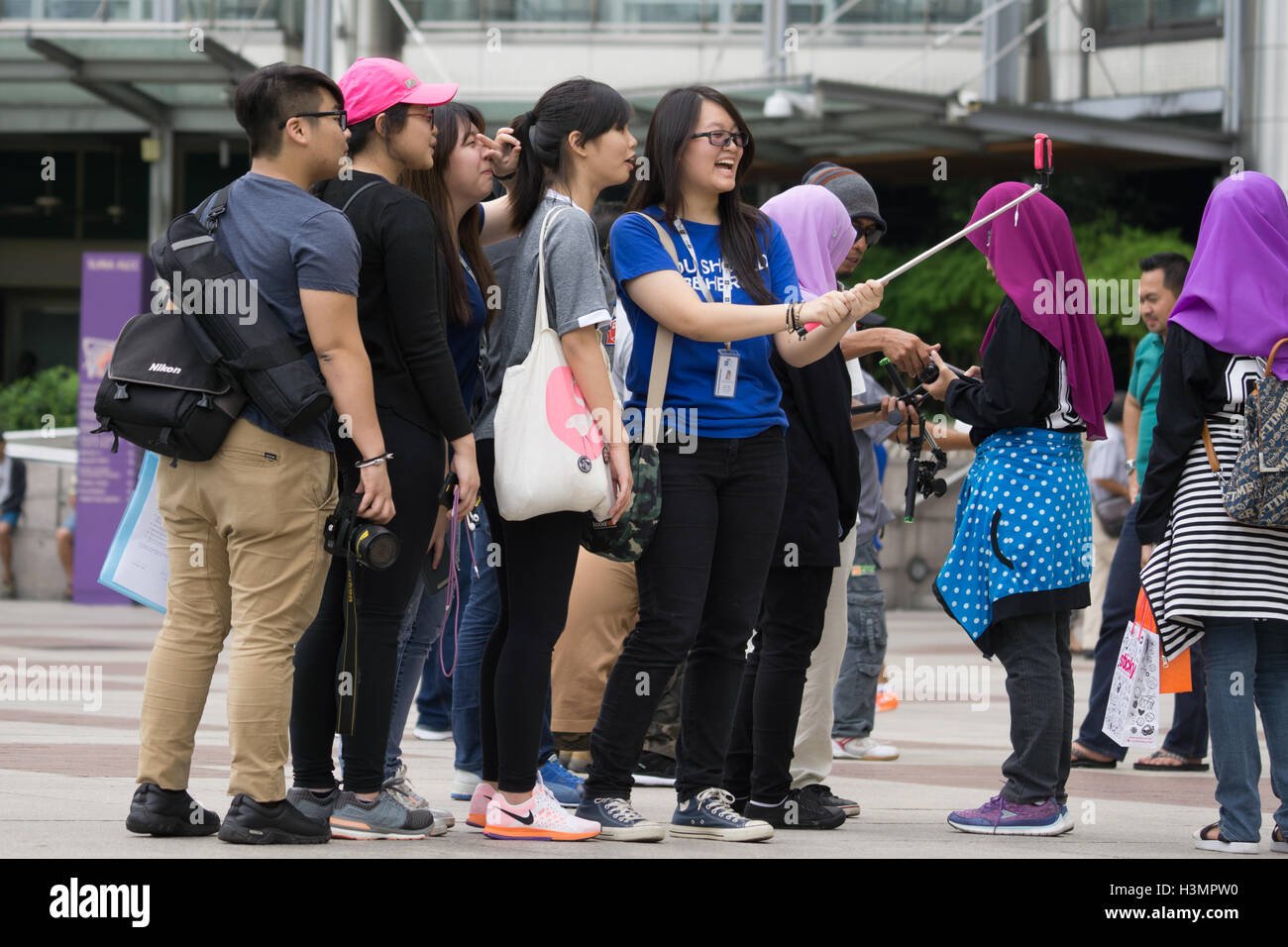 A girl takes a group Selfiie using a Selfie Stick and a mobile phone near to the Petronas Twin Towers,Kuala Lumpur,Malaysia Stock Photo