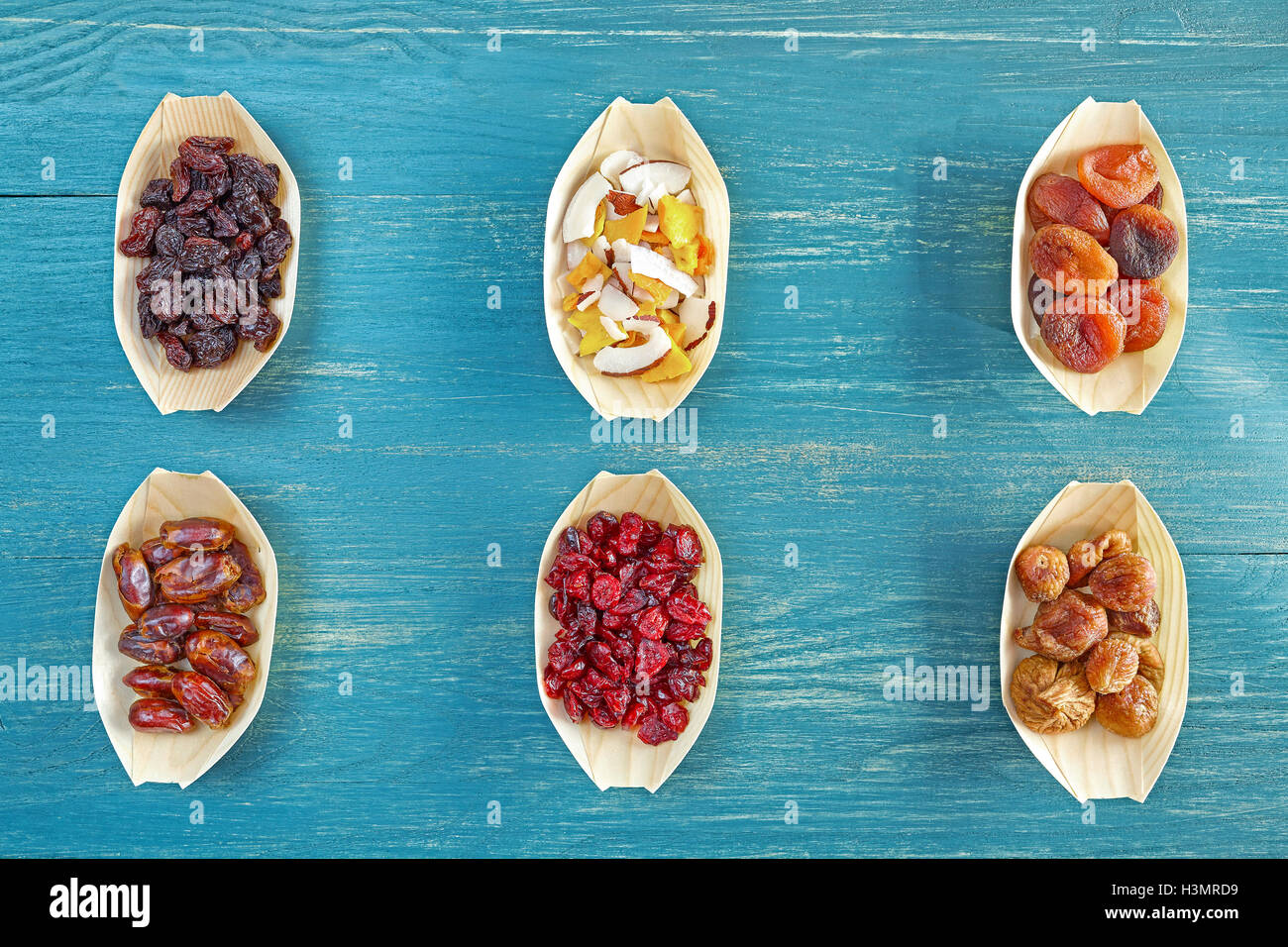 Dried fruits selection in wooden bowls on blue rustic table, view from above. Stock Photo