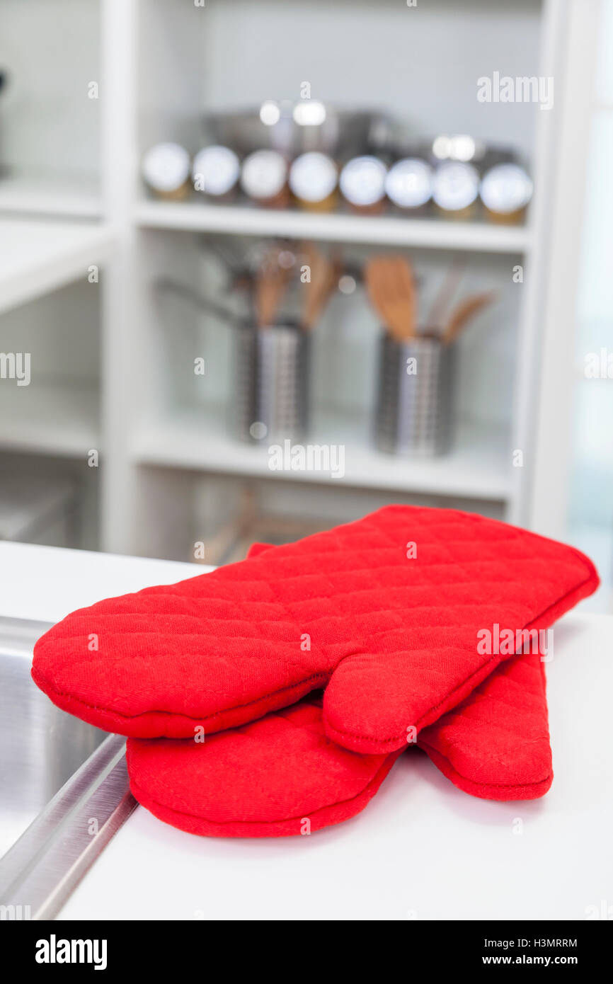 Red oven gloves or mitts on the counter top in a modern home kitchen Stock Photo