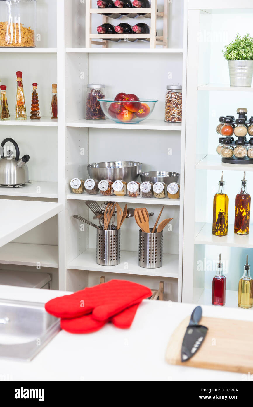 A modern kitchen empty no people, with red oven gloves, oils, olive oil, wine, fruit, spices, equipment, utensils, kettle, knife Stock Photo