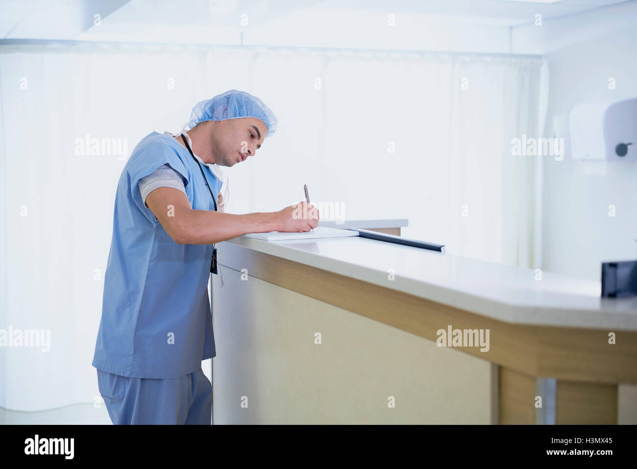 Male doctor writing in medical notes at nurses station in hospital Stock Photo